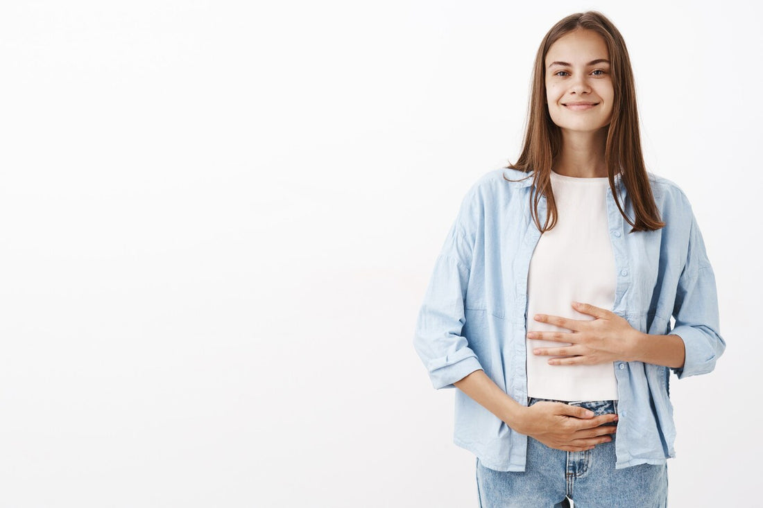 Happy young woman smiling while touching her stomach, promoting gut health with vitamins or yogurt.