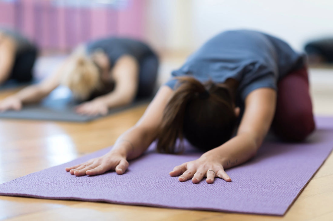 Yoga class participants practice Child’s Pose on yoga mats to promote relaxation and circulation for managing POTS.