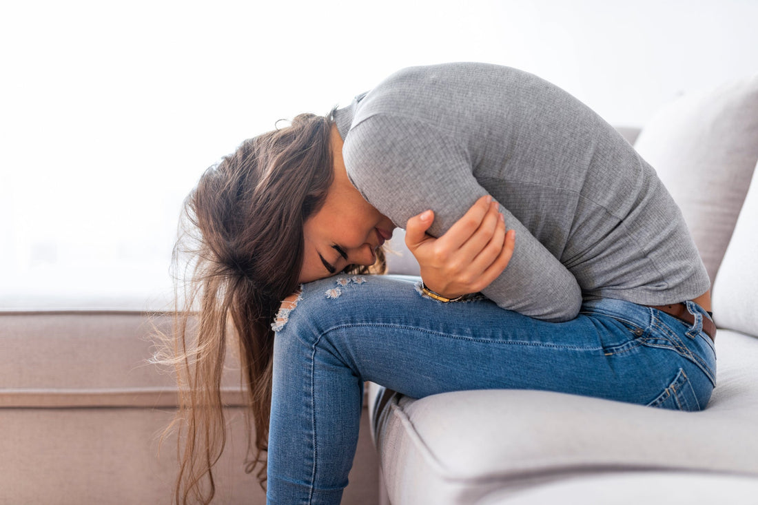 Woman sitting on a couch holding her stomach, showing discomfort from gastrointestinal symptoms in POTS.