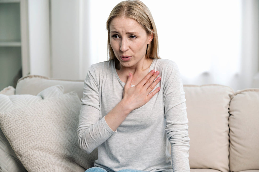 A woman sits on a couch trying to calm heart palpitations and discomfort caused by POTS and autonomic nervous system dysfunction.
