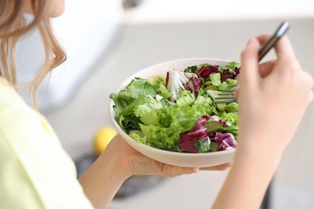 A person eats a bowl of fresh green salad with mixed leafy greens and purple vegetables, demonstrating a vegan meal option.