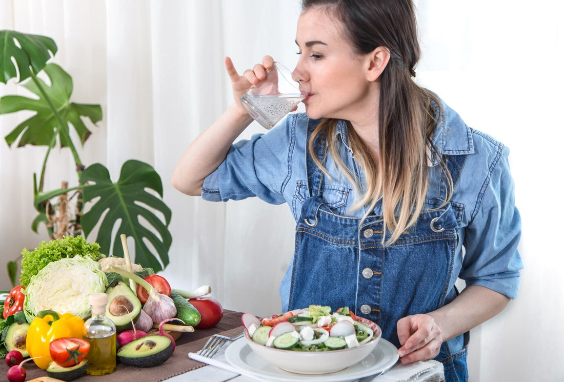Young woman drinking water at the table with vegetables