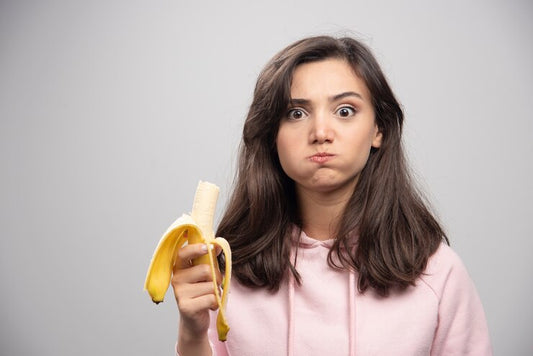 Young woman eating banana over gray wall.