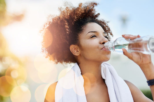 A woman drinks a bottle of water with a squeeze of Buoy electrolyte and mineral drops for optimal weight loss.