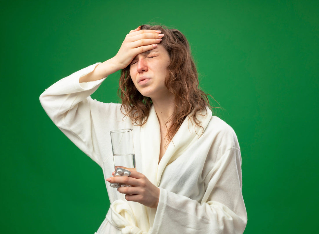 Woman holding a glass of water with hand on forehead showing migraine pain linked to dehydration and electrolyte imbalance