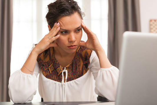 Woman at a laptop pressing her temples, showing migraine-related pain, tension, and difficulty focusing.