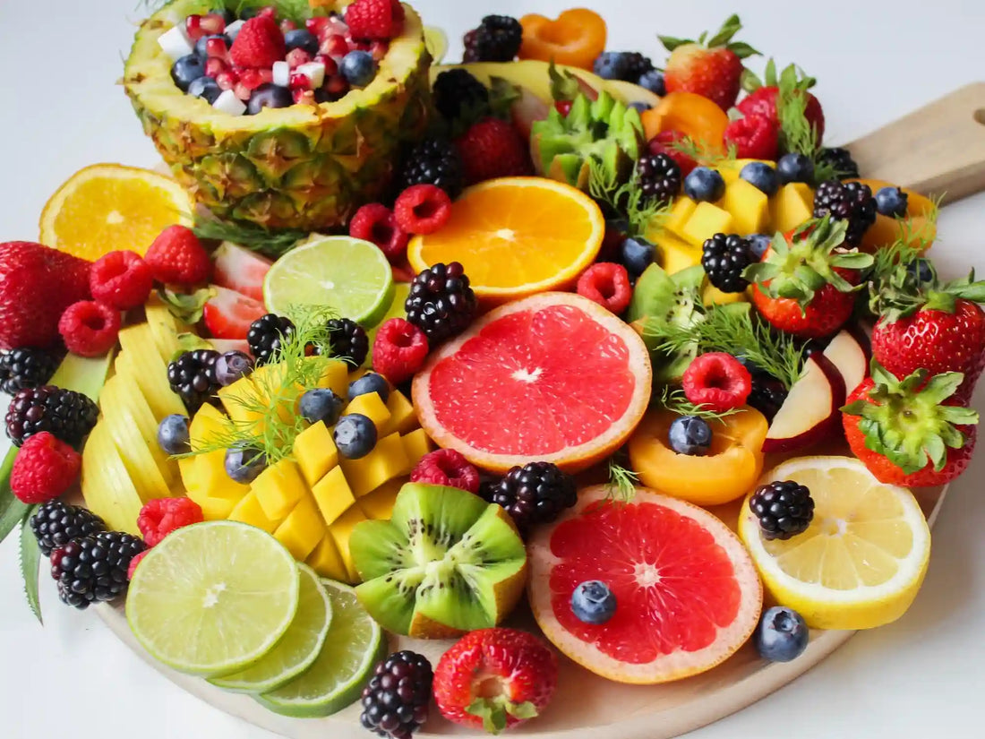 A vibrant platter overflowing with electrolyte-rich fruits—grapefruit halves, lime and lemon slices, fresh strawberries, blueberries, blackberries, raspberries, kiwi, mango cubes, pineapple, and apricots—arranged on a wooden board.