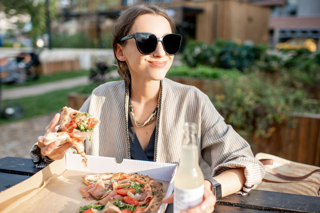 A woman enjoys a piece of pizza with prosciutto for a high-sodium snack that will help manage her POTS symptoms.