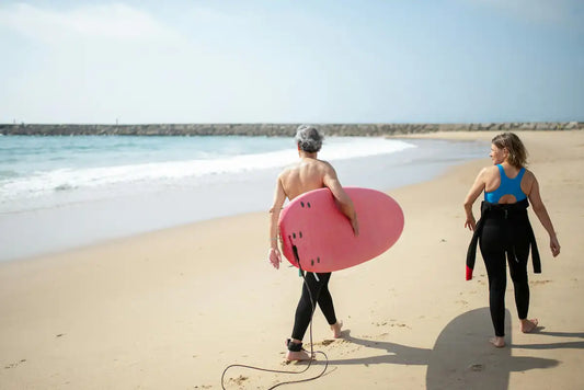 older adults carrying surfboards on the beach