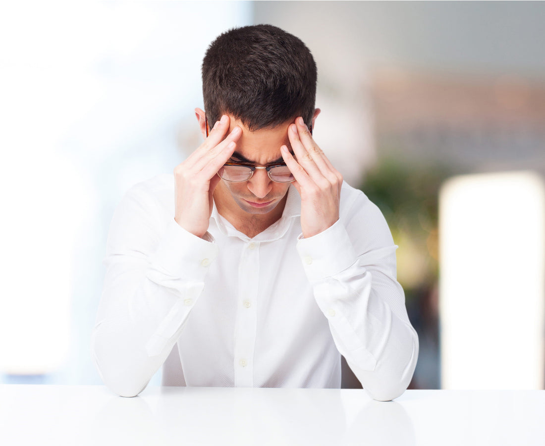 Man experiencing migraine brain fog and headache while holding his temples at a desk