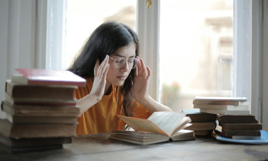 Young woman reading a book while touching her head, showing signs of fatigue and a headache.
