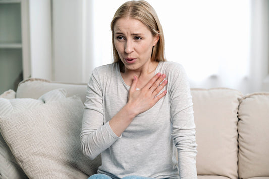 A woman sits on a couch trying to calm heart palpitations and discomfort caused by POTS and autonomic nervous system dysfunction.