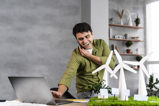 Man smiling and working at his desk while talking on the phone and using a laptop, showing energy and focus during a productive workday.