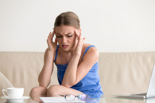 Woman sitting on couch holding temples while experiencing a migraine headache and sensitivity indoors