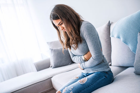 A woman sits holding her stomach due to pain from POTS comorbidities.