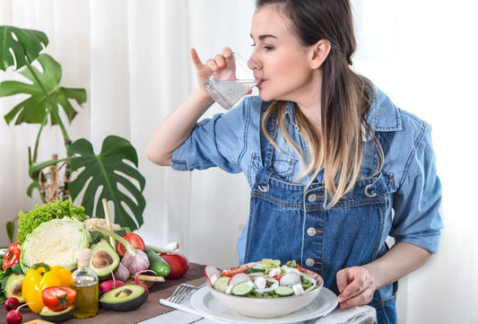 Young woman drinking water at the table with vegetables